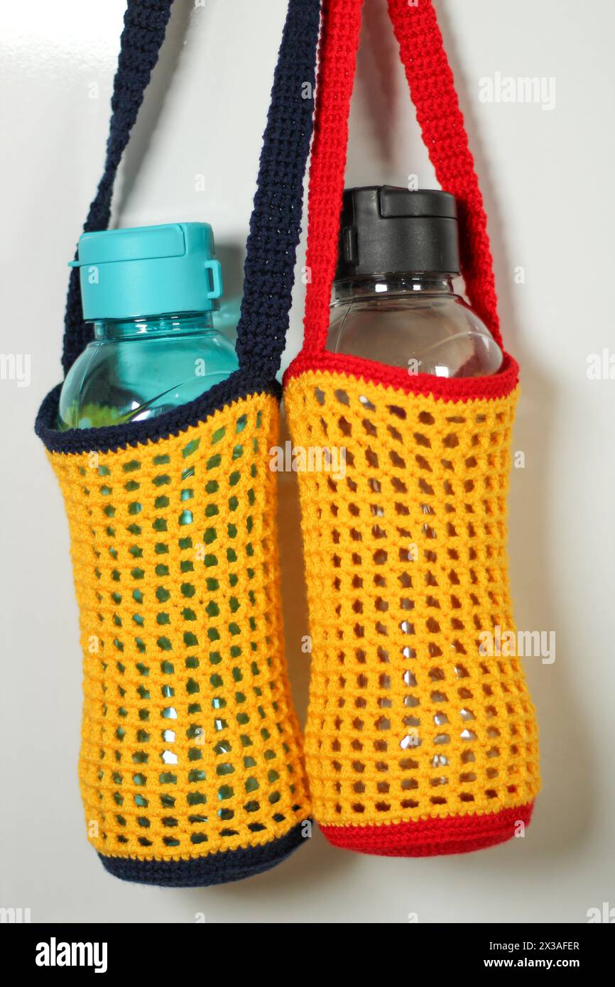 Knitted red, yellow and blue drinking water bottle holder isolated on white background. Stock Photo