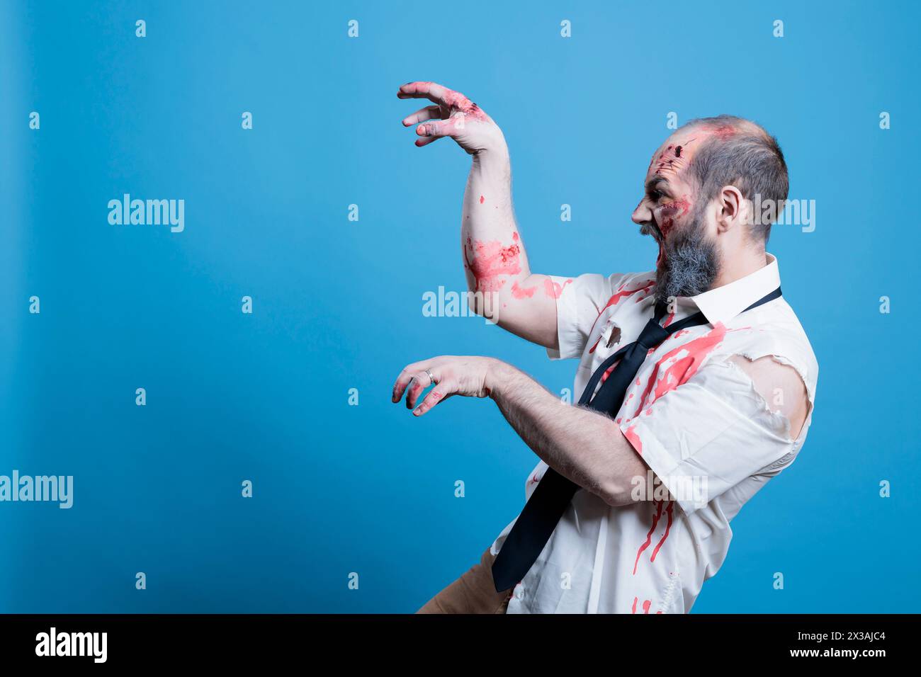 Starving undead zombie hissing and looking for human brains, haunting victims. Walking dead cadaver searching for flesh to consume, preparing for attack with hands acting as claws, studio background Stock Photo