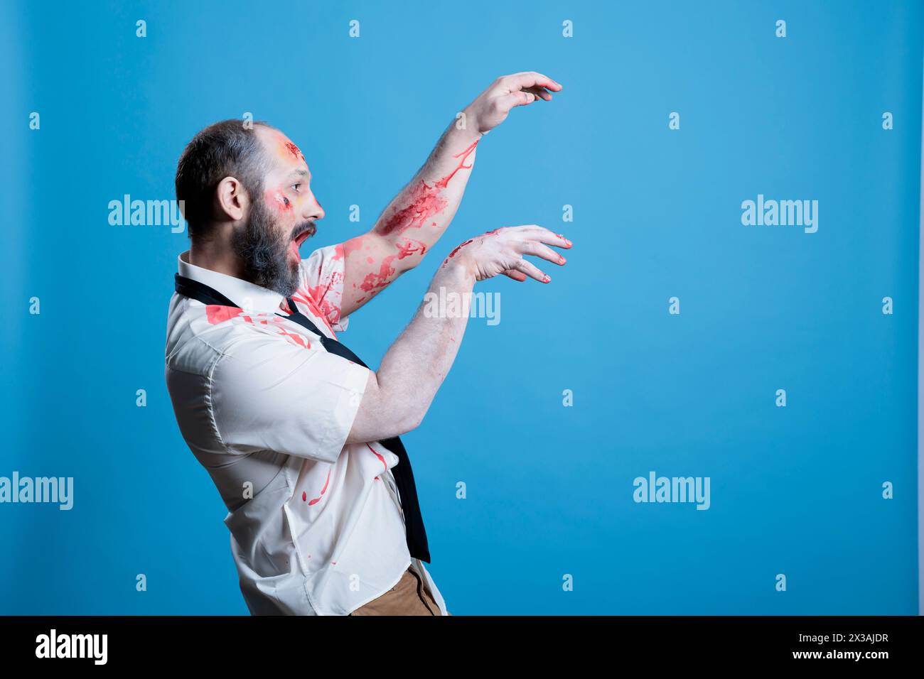 Possessed man covered in blood turned into zombie after being killed, haunting place. Wounded ghoulish cadaver limply walking towards victim, preparing for attack, studio background Stock Photo