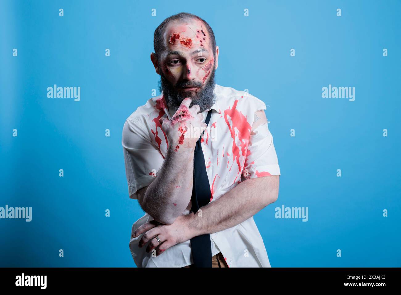 Actor dressed as horror movie brainless zombie repeating lines between scenes on set. Man costumed as mindless infected creature preparing for role, isolated over studio background Stock Photo