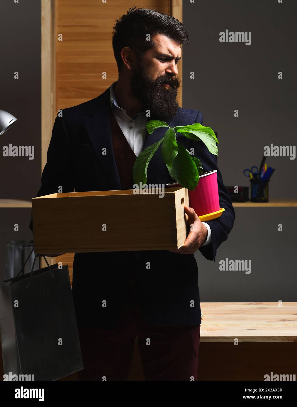 Losing job. Upset office worker is fired. Unemployment. Dismissed employee leaving office with box of his belongings. Sad bearded man in suit with box Stock Photo