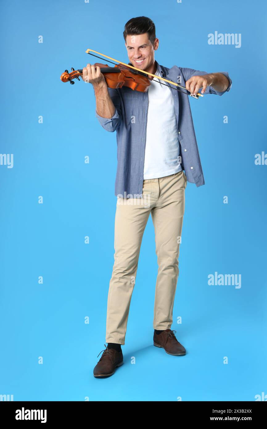 Happy man playing violin on light blue background Stock Photo