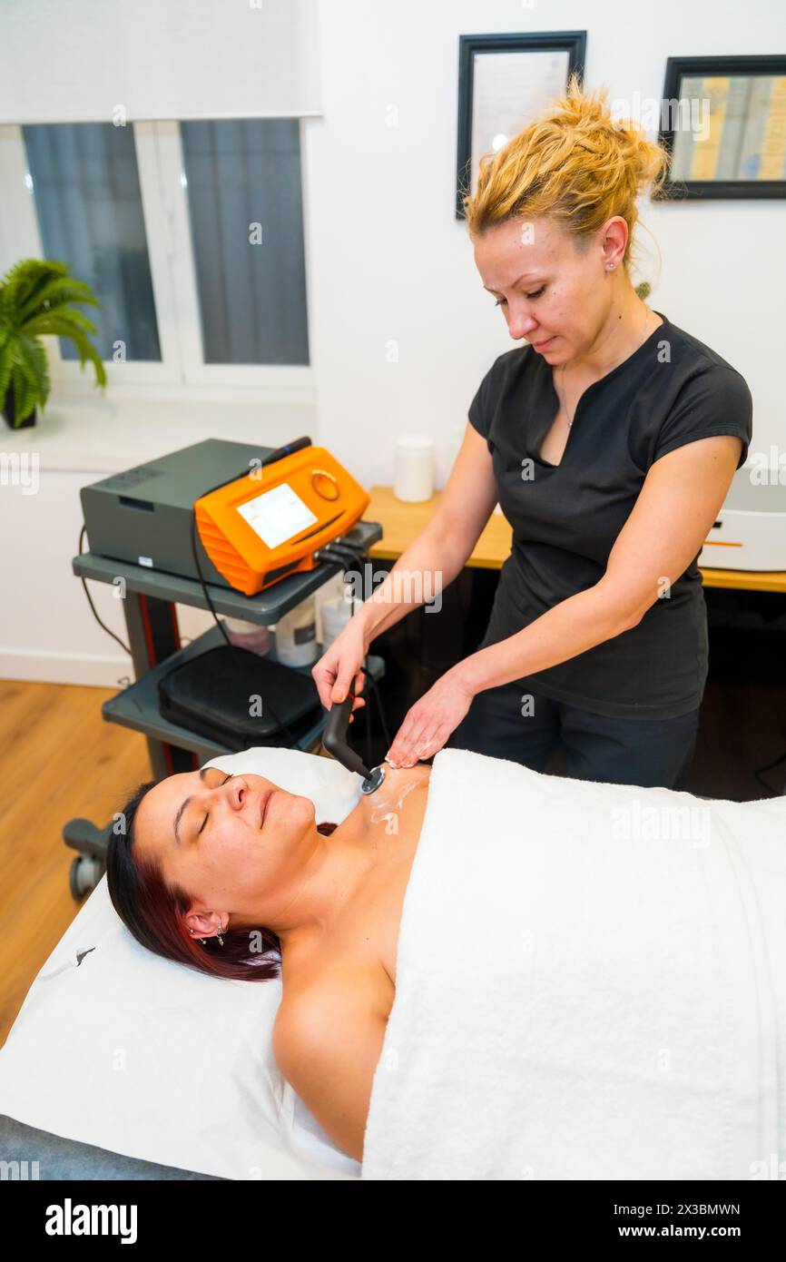 Vertical side view of a female beauty patient lying on massage table receiving indiba treatment Stock Photo