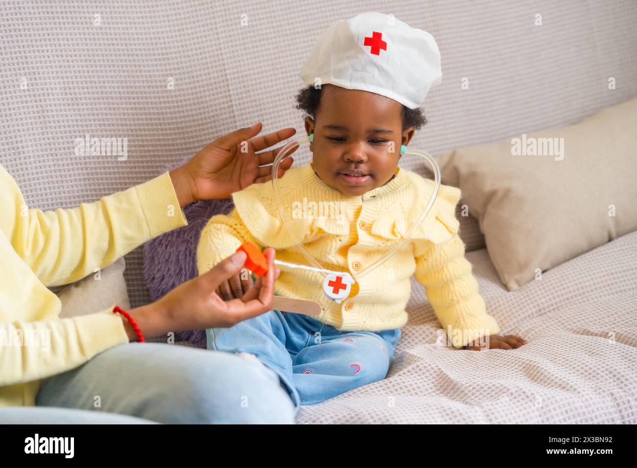 Horizontal cropped photo of an African little child playing doctors with her mother on the sofa Stock Photo