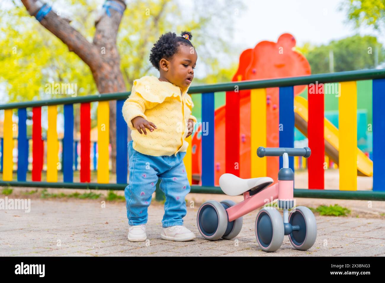 Full length photo of an african baby girl in a playground with a toy bike alone Stock Photo