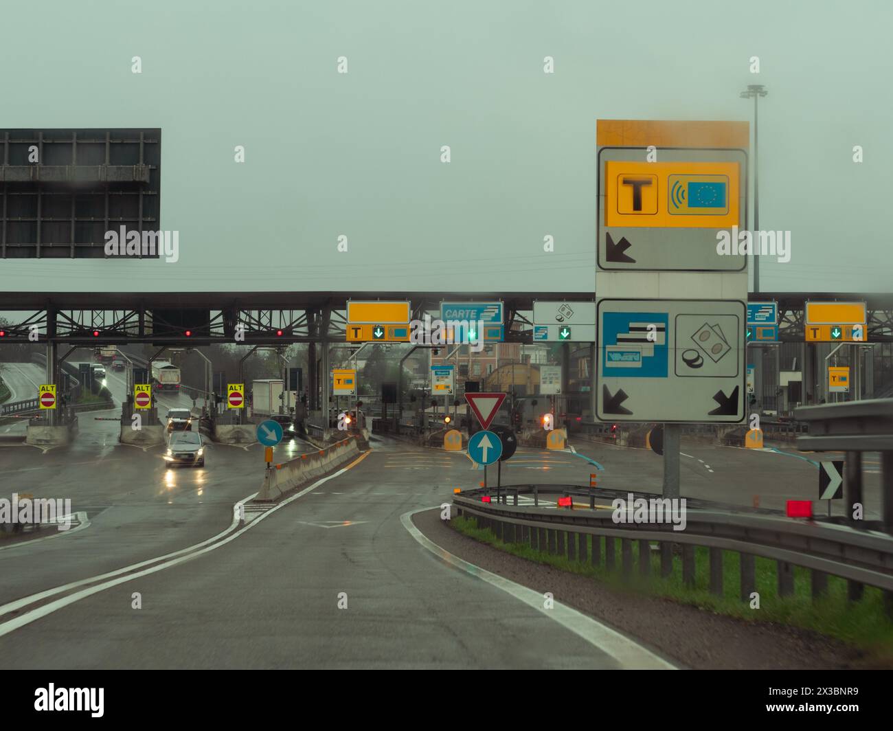 Cars approaching toll booths on a wet road with traffic signs overhead ...