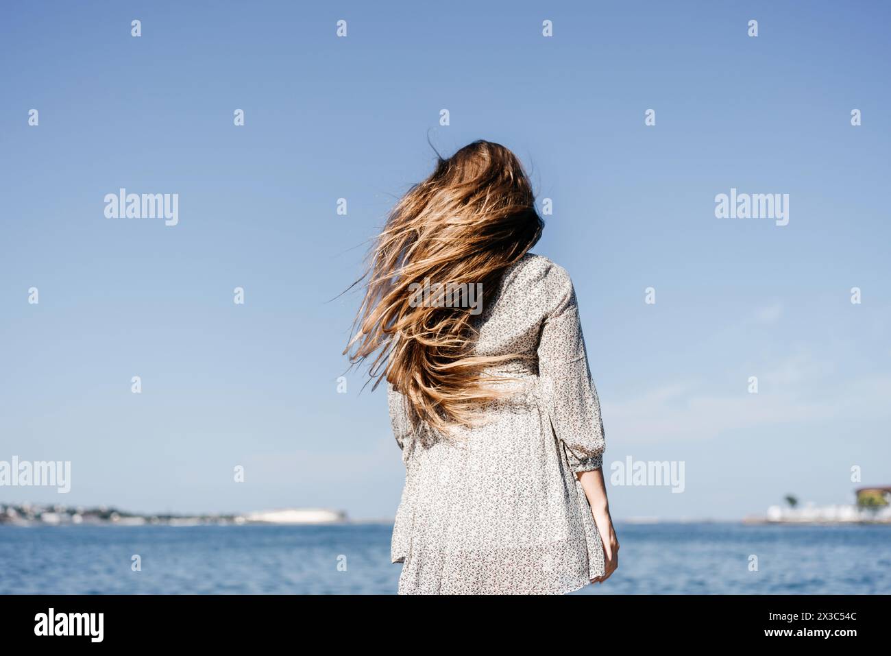 woman with long hair stands in front of a blue sky. She is wearing a ...