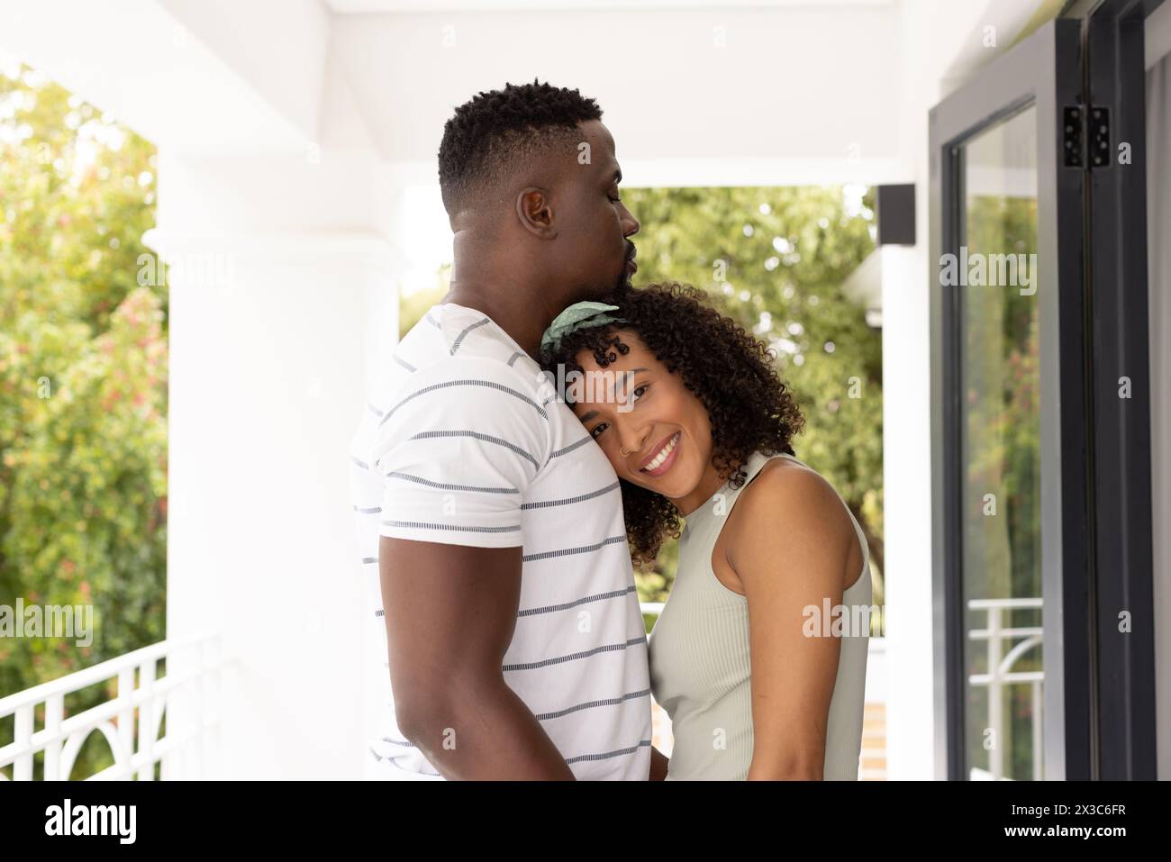 Diverse couple embracing, standing on front porch Stock Photo