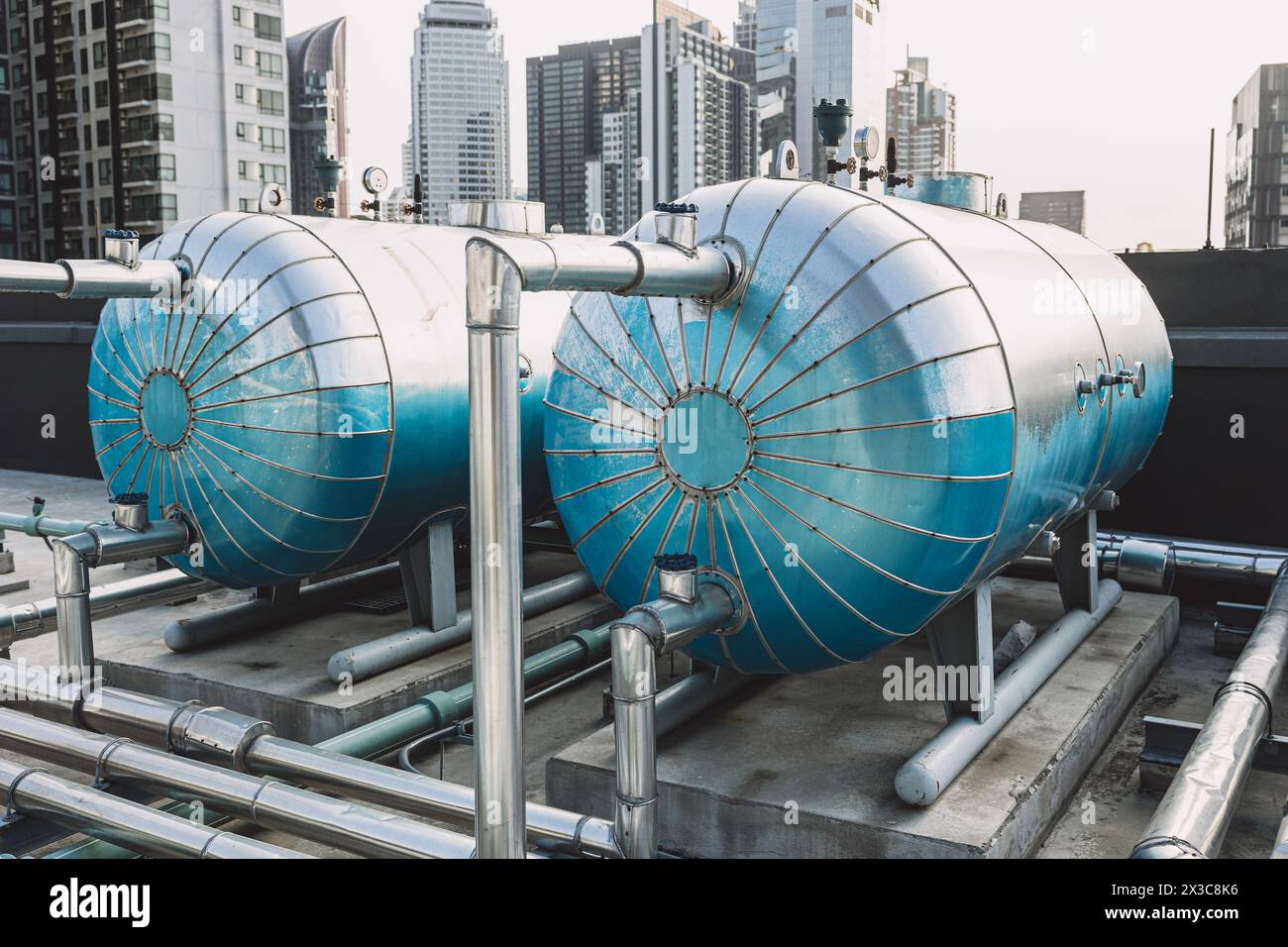 Stainless Steel Insulated Large Hot Water Storage Pressure Tank for hotel at outdoor roof top with hot water pipe heat pump system. Stock Photo