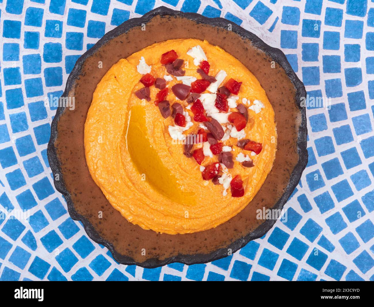 Htipiti, a Greek appetizer based on feta cheese and roasted red peppers, in a ceramic bowl, on a blue and white mosaic table, top view, flat lay Stock Photo