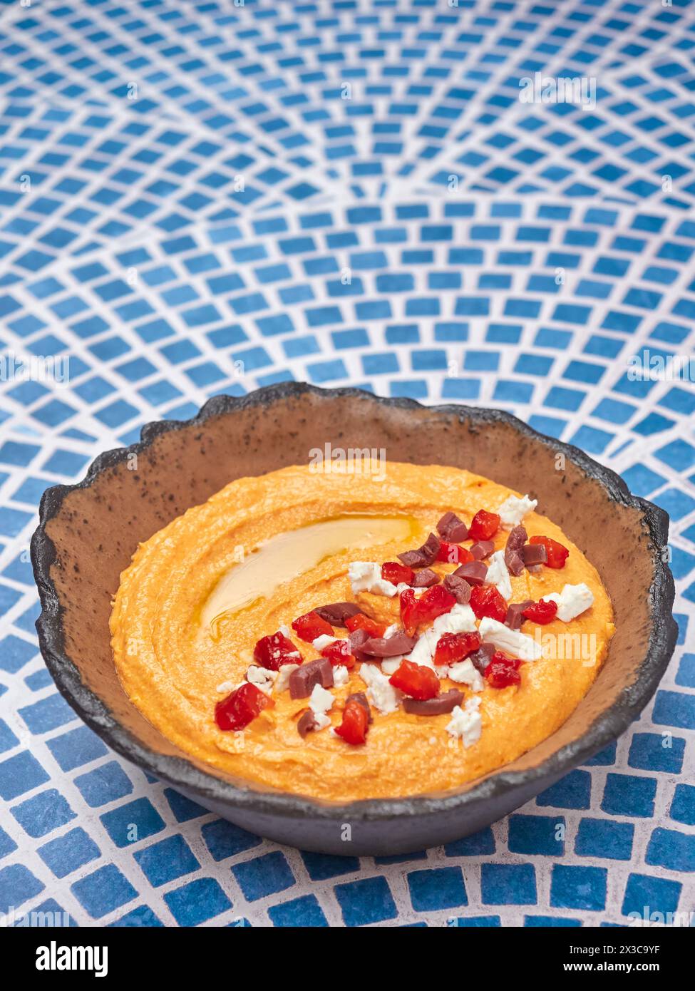 Htipiti, a Greek appetizer based on feta cheese and roasted red peppers, in a ceramic bowl, on a blue and white mosaic table, top copy space Stock Photo