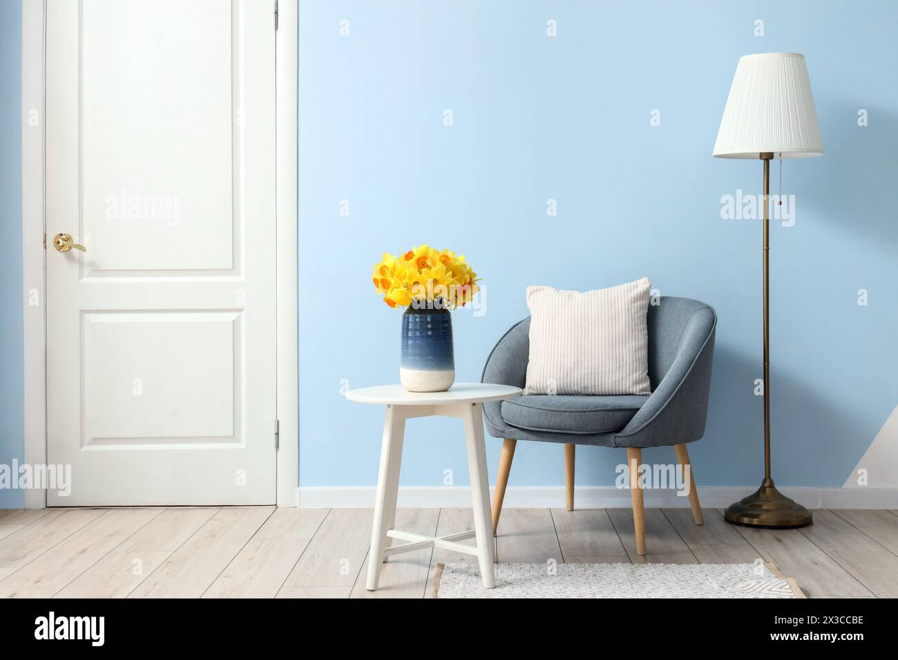 Armchair and coffee table with vase of narcissus flowers in blue living ...