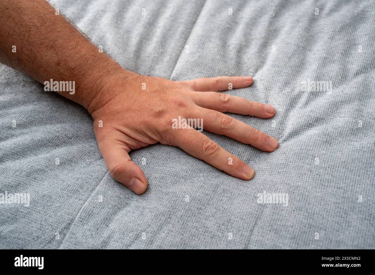 The man checks the quality and softness of the new mattress he will buy by pressing it with his hand Stock Photo