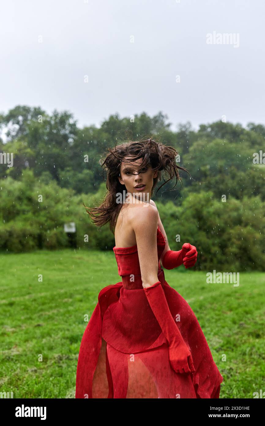 An elegant young woman in a flowing red dress and long gloves stands ...
