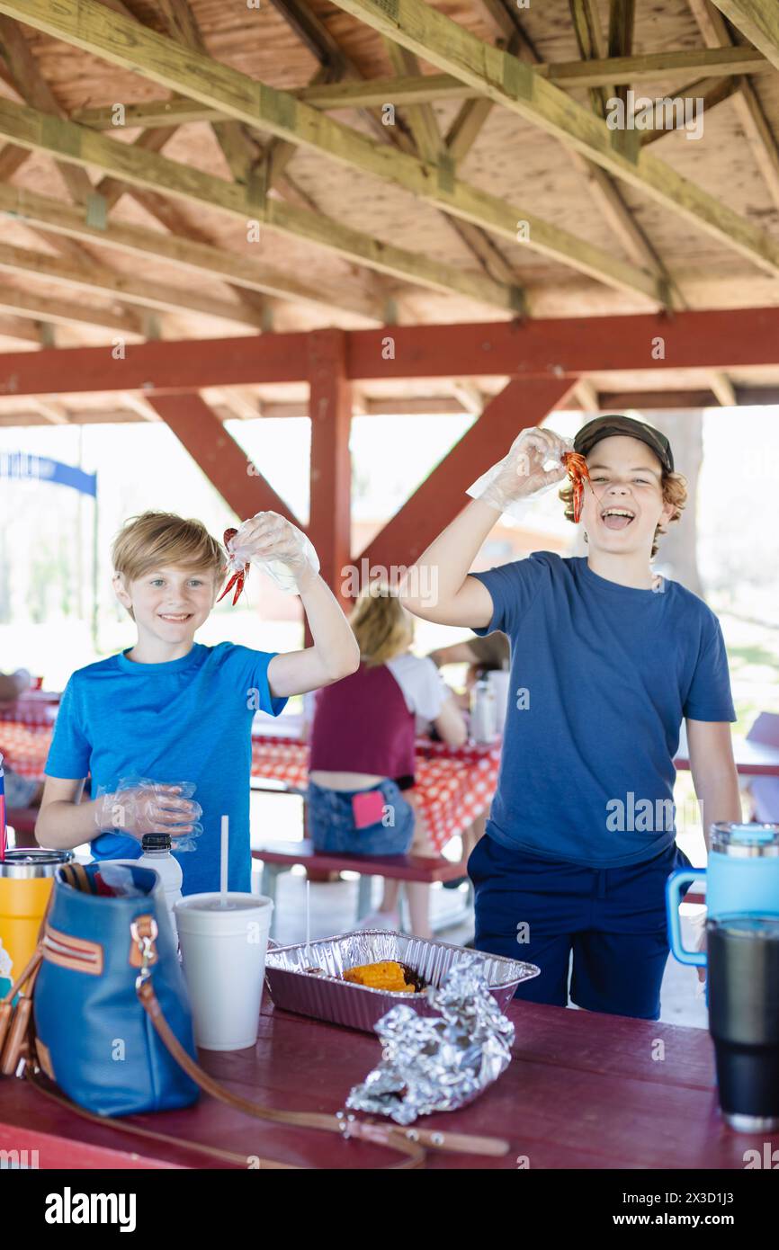 Boys share laughs holding crawfish at a sunny picnic Stock Photo