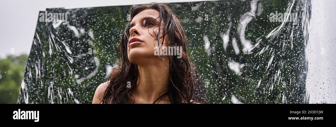 A young woman in a red dress stands before a mirror covered in water ...