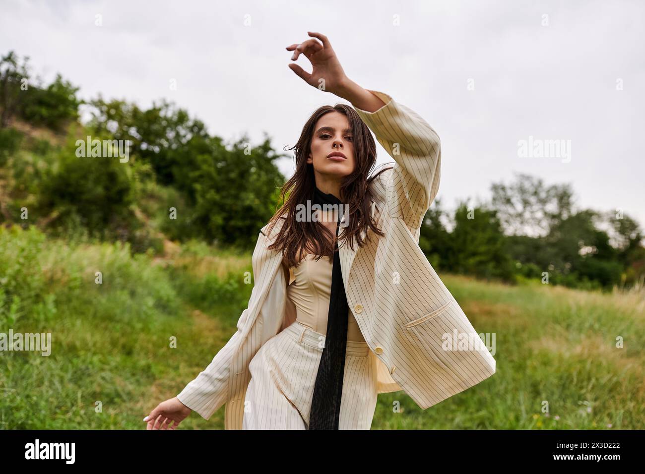 A beautiful young woman in white attire stands elegantly in a field, feeling the summer breeze gently caress her. Stock Photo