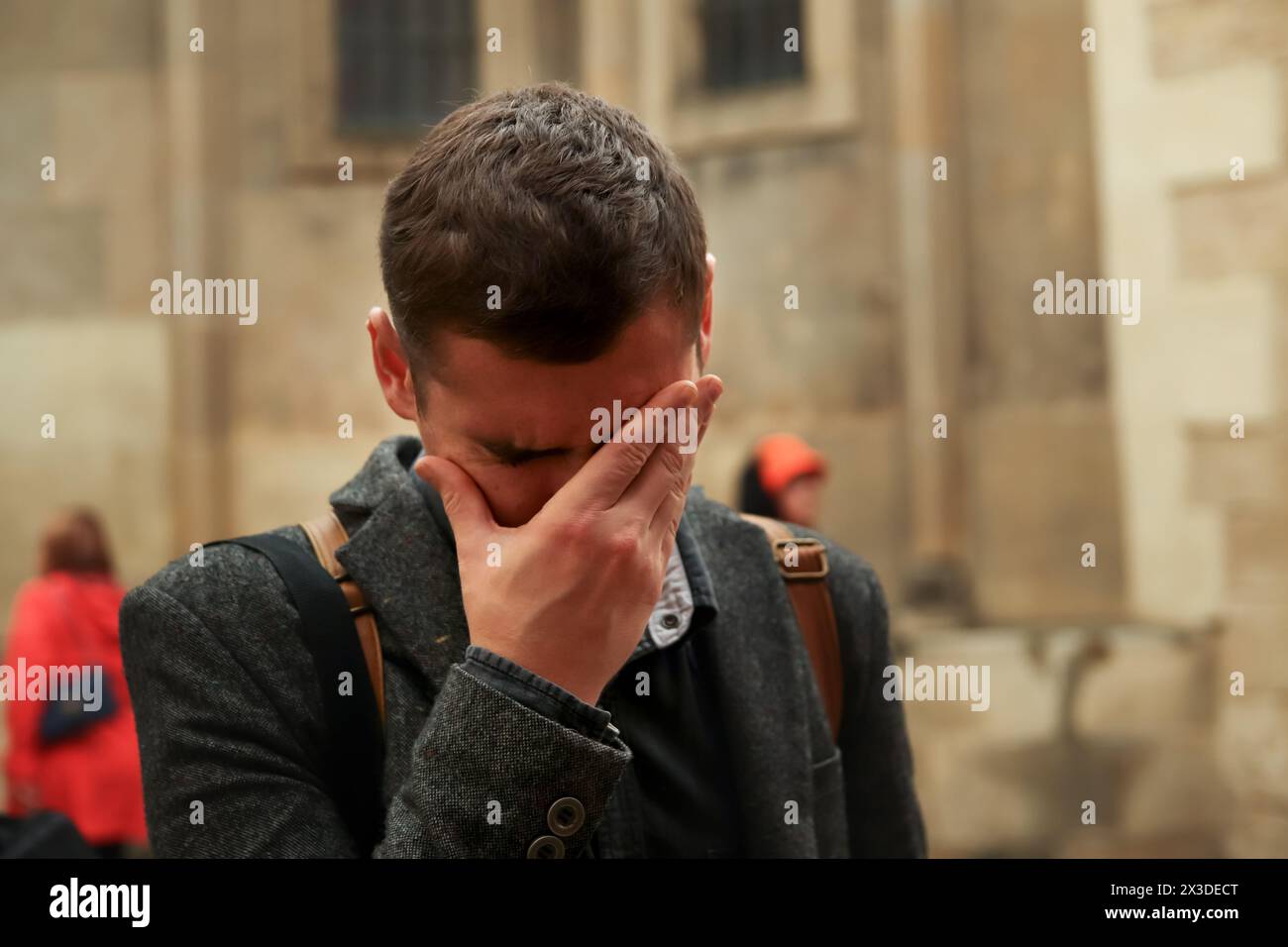 Young man outside, expressing fatigue and stress with a facepalm gesture. Concept of burnout: man showing signs of stress and fatigue, holding his hea Stock Photo