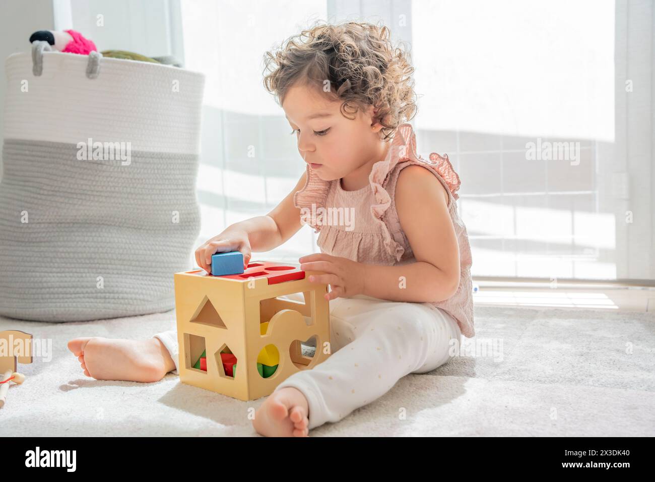 cute little girl with curly hair sitting on the floor playing with cube of wooden colorful pieces and shapes. montessori materials. concept developmen Stock Photo