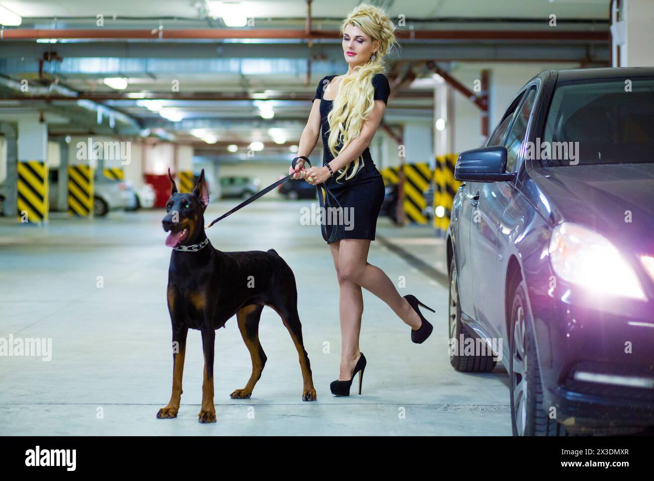 MOSCOW - JUN 01, 2015: Girl (with model release) with long blond hair in dress with the Doberman on leash in the underground parking Stock Photo