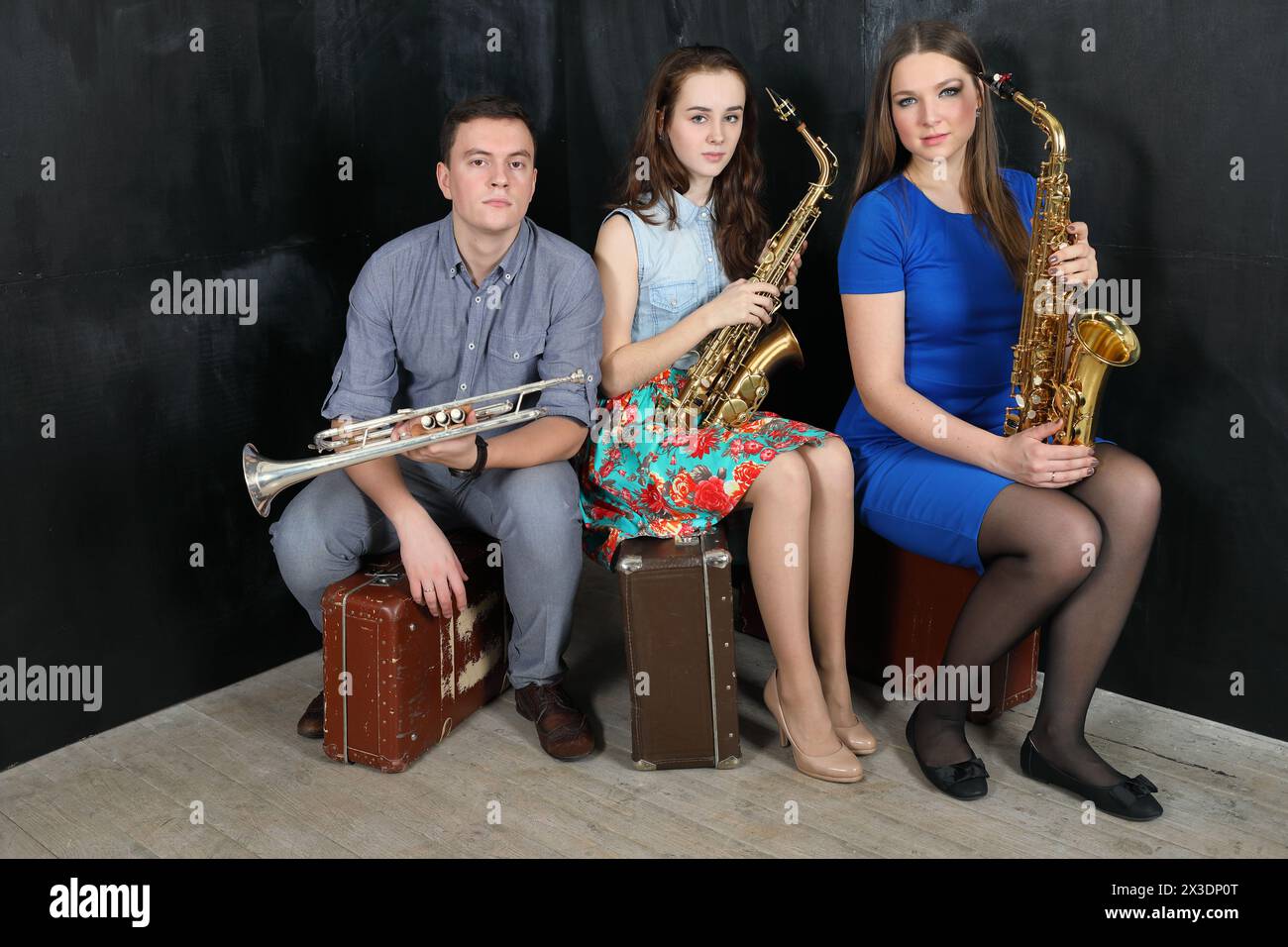 Three musicians with wind instruments in their hands sitting on old suitcases Stock Photo