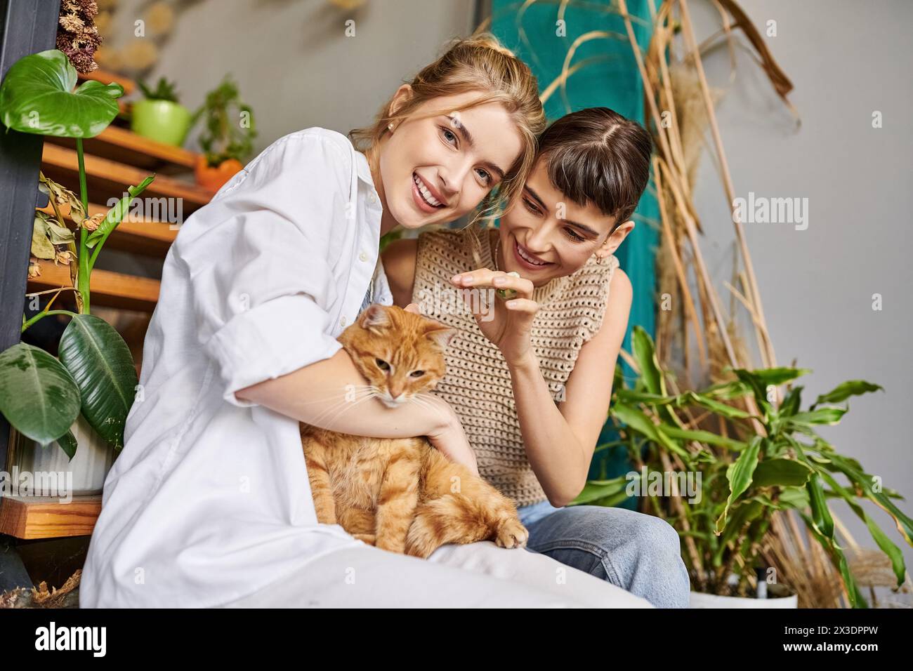 Two women sit on a bench, accompanied by a cat. Stock Photo