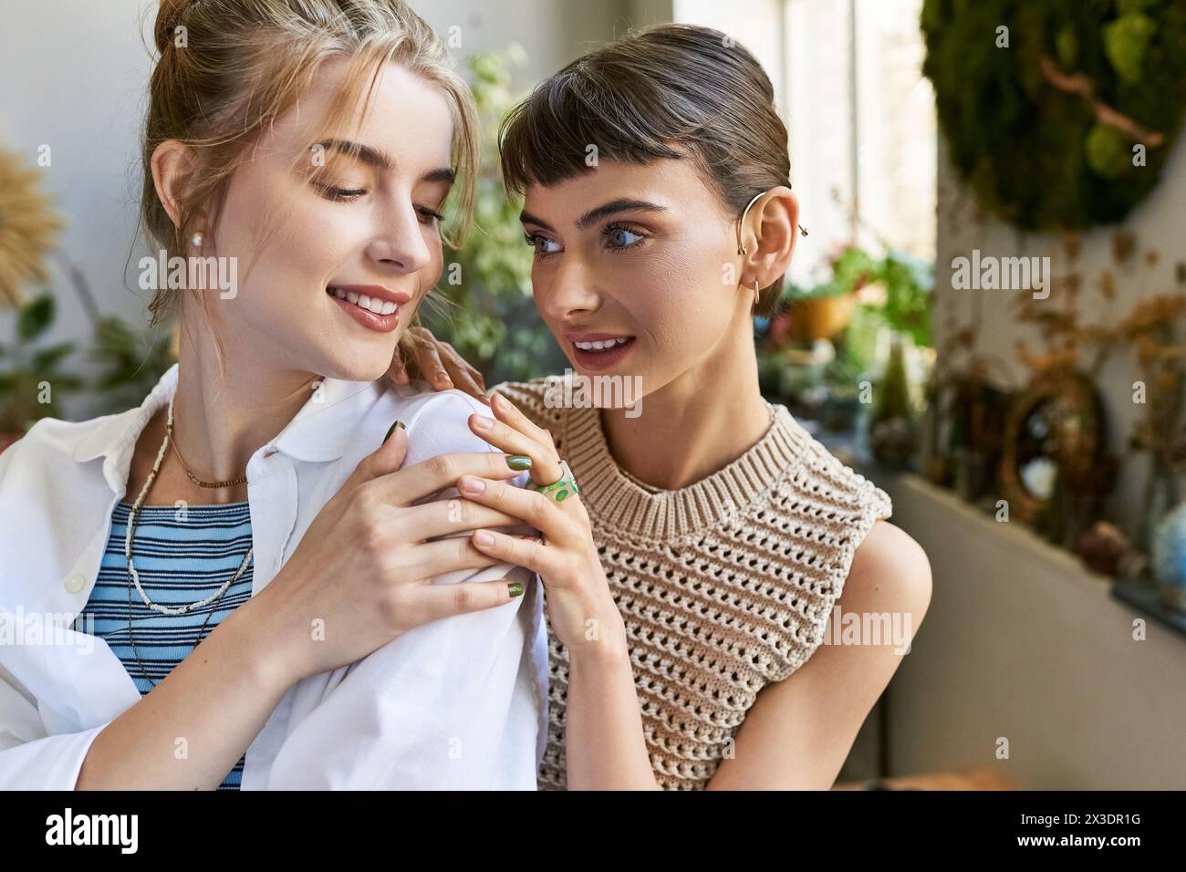 Two young women, one with short hair and the other with long hair, stand side by side in an art studio, sharing a tender moment. Stock Photo