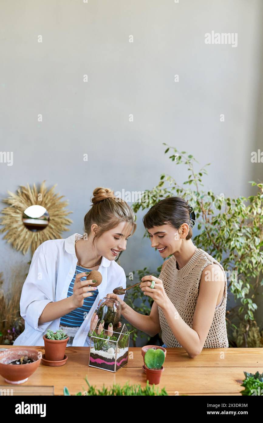 Two women, sharing a moment at a table surrounded by plants in an art studio. Stock Photo