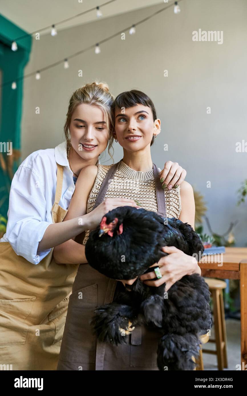 Two women, a loving lesbian couple, standing together in an art studio, holding hen. Stock Photo
