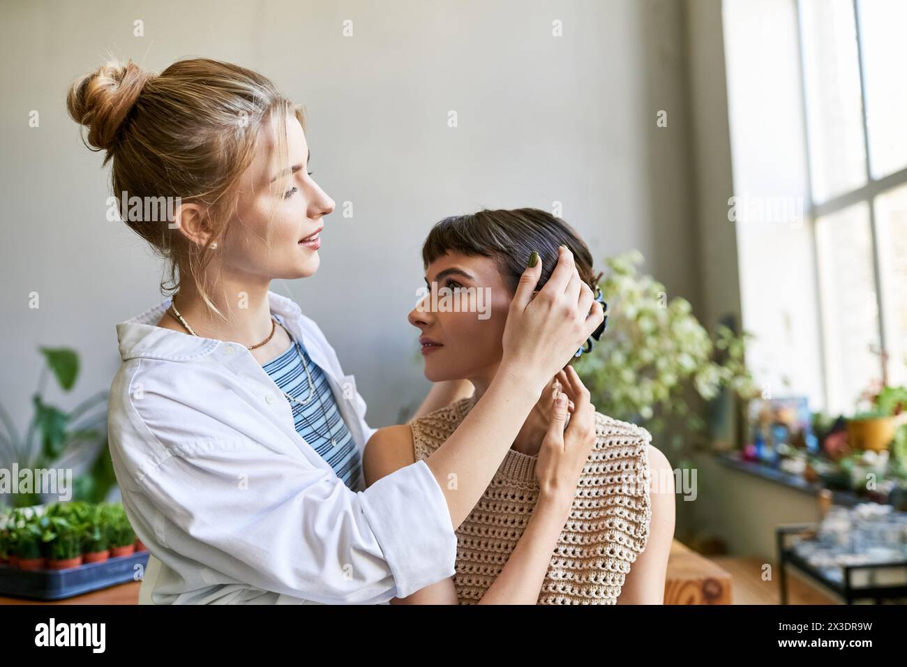 A woman lovingly styles another womans hair in an art studio. Stock Photo