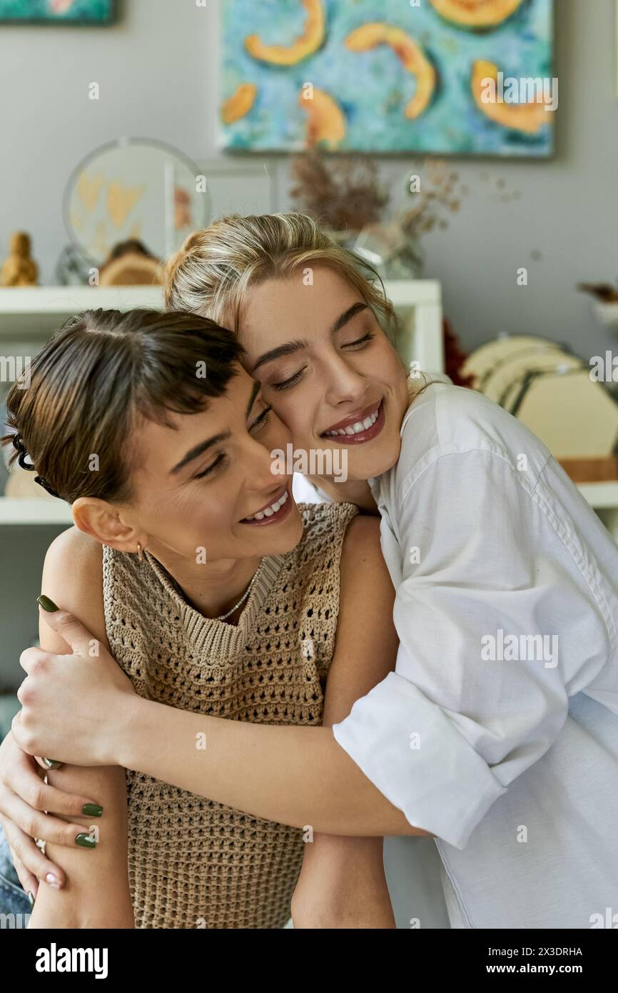 Two women, a loving lesbian couple, share a tender hug in an art studio. Stock Photo