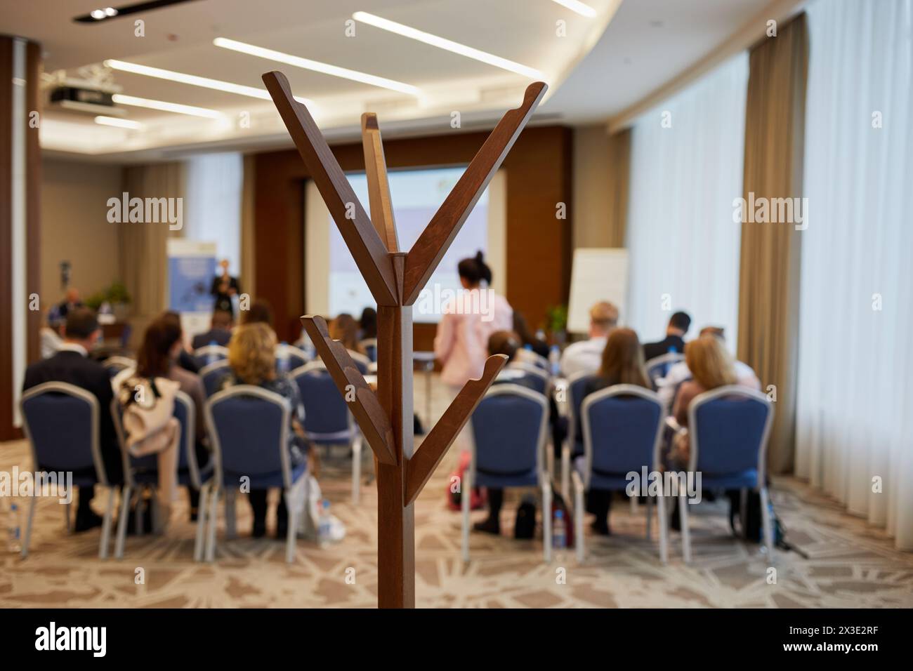 Wooden hat and coat stand in room with people sitting on chairs, shallow dof. Stock Photo