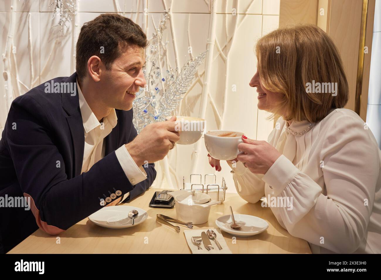 Smiling man and woman sit at table in cafe talking and drinking coffee. Stock Photo