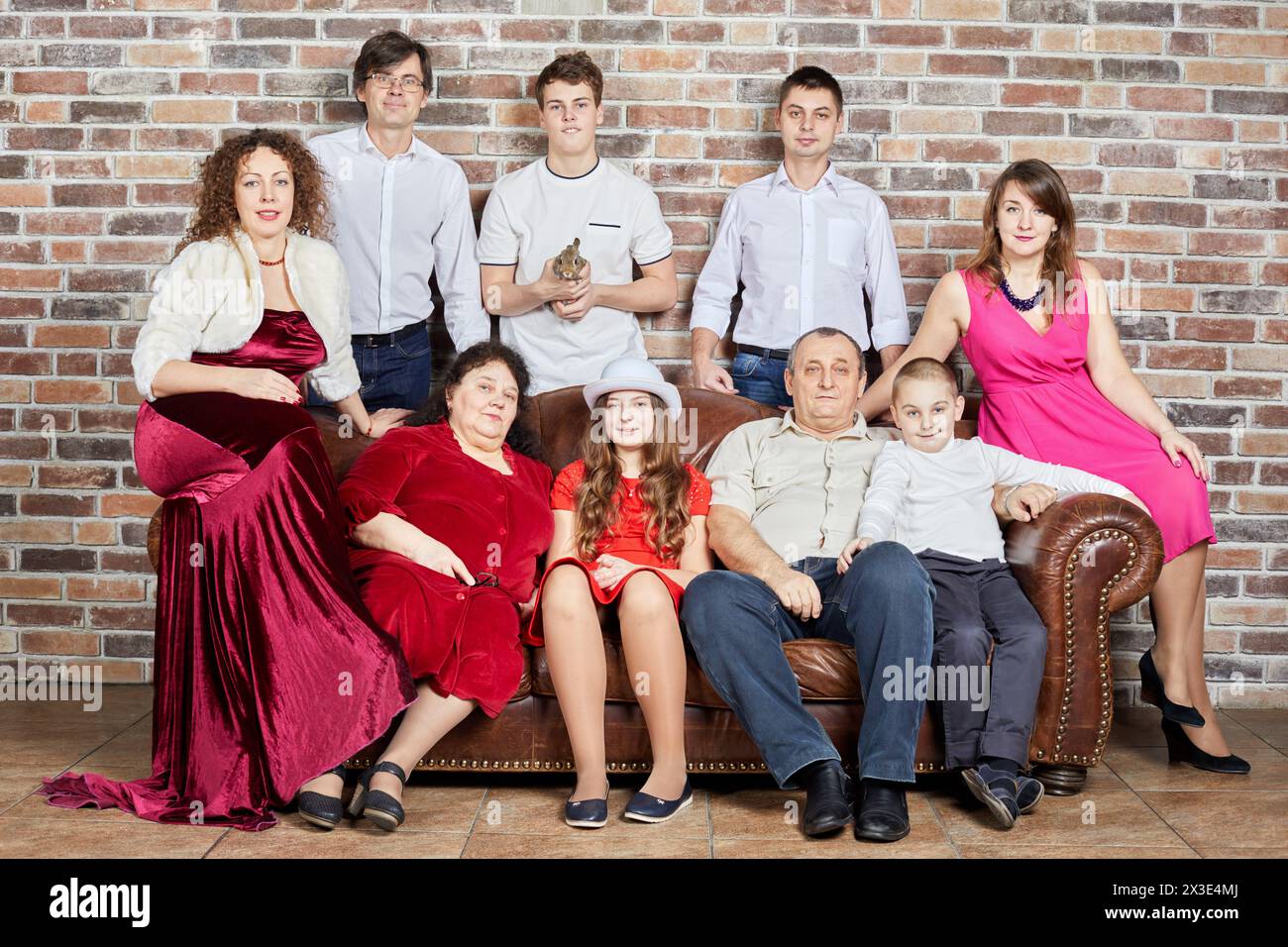 Group portrait of large family around old leather sofa at red bricks wall. Stock Photo