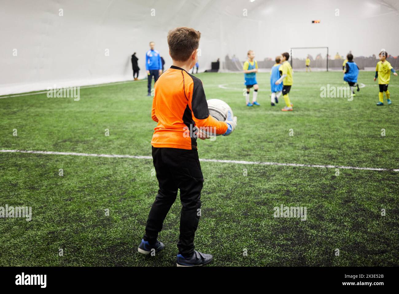 Boy goalkeeper going to put the ball into play, rear side view. Stock Photo