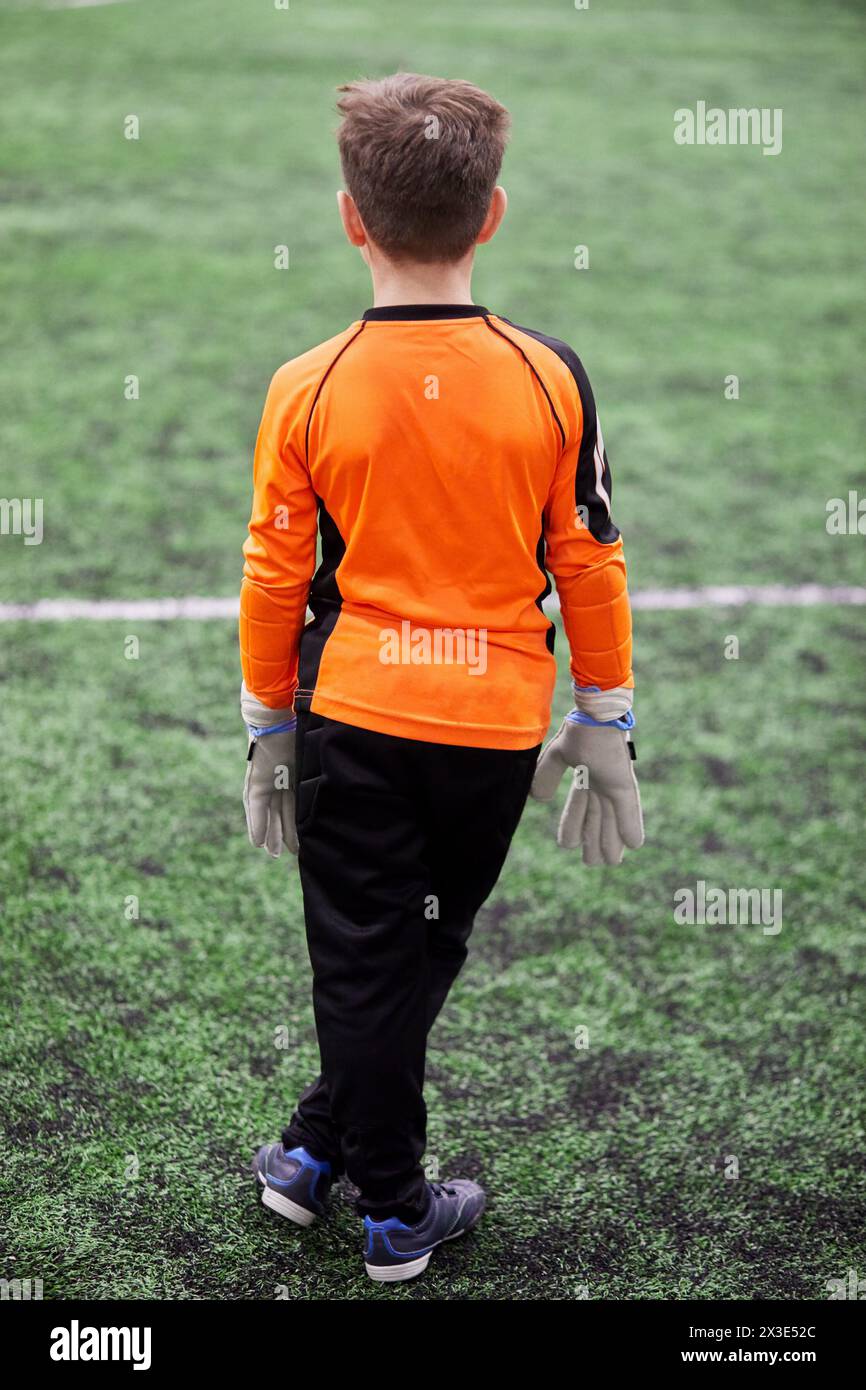 Boy goalkeeper stands in goal box on sports playground, rear view. Stock Photo