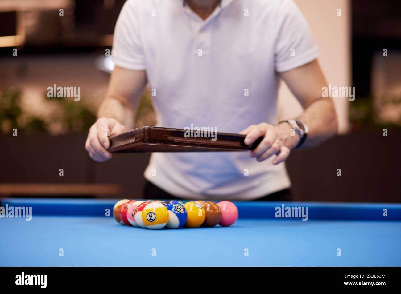 Man in white shirt arranges pool balls on table in club. Stock Photo