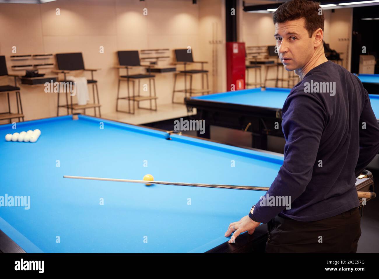 Man At Pool Table Man in dark blue shirt stands half-turned at pool table with balls ...