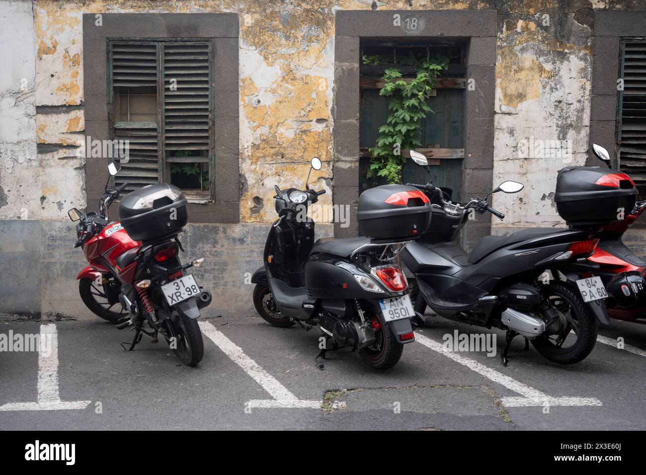 Scooters and bikes parked in front of the rotting windows and walls of a derelict property, on 18th April 2024, in Funchal, Madeira, Portugal. Stock Photo