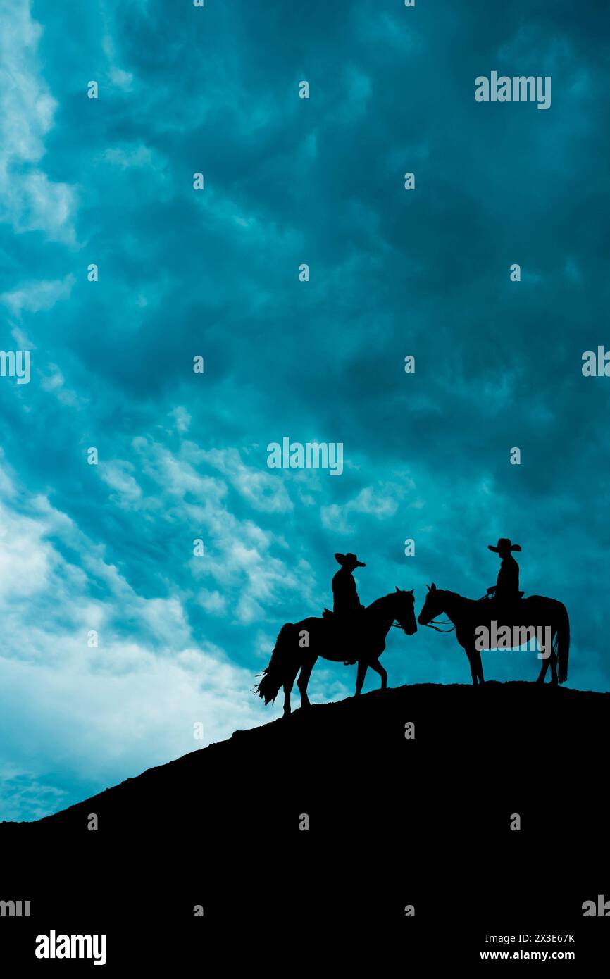 silhouette of two cowboys on horses standing on a hill Stock Photo