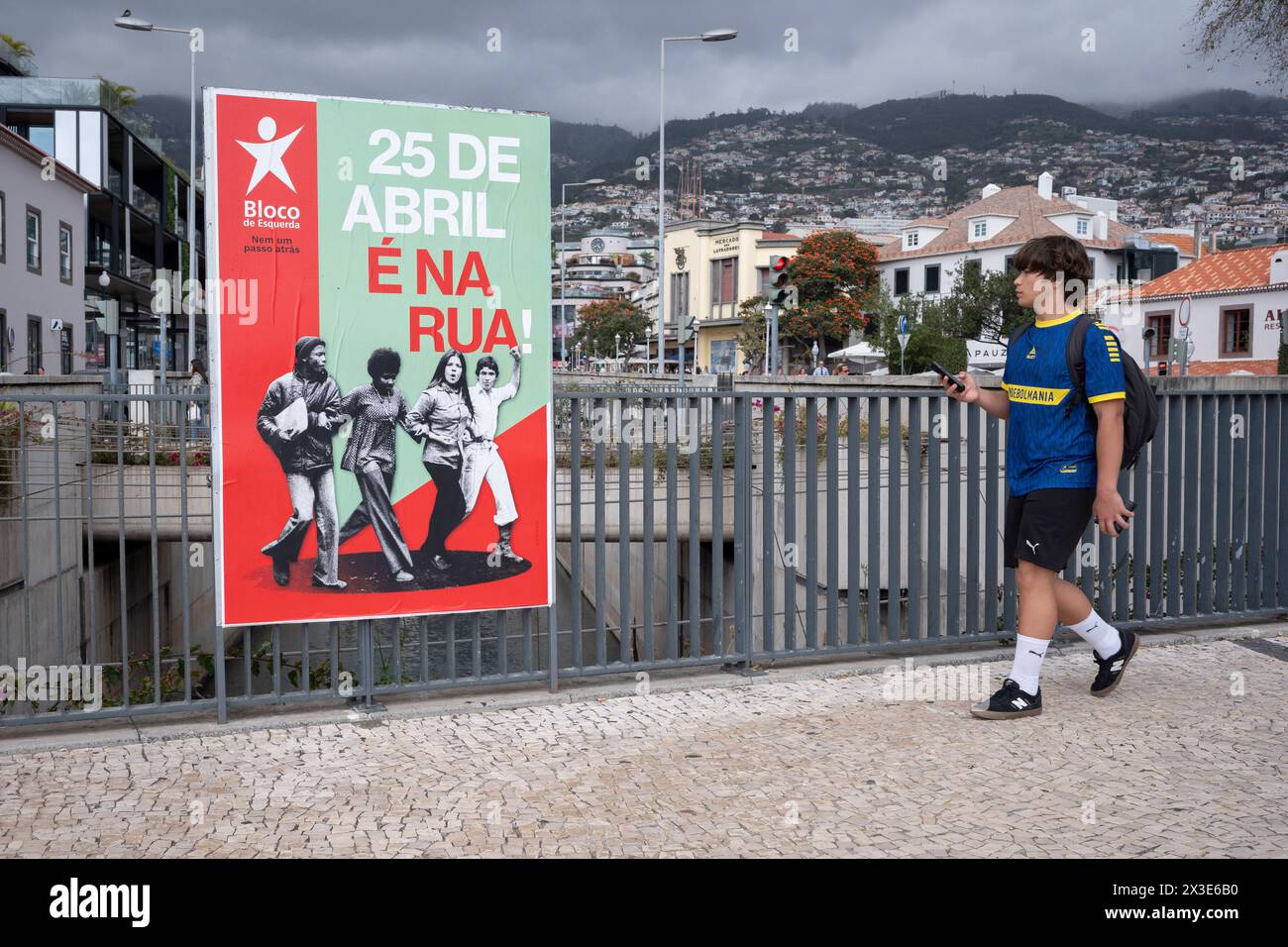 A young Portuguese man walks past a poster by the 'Bloco de Esquerda' political party celebrating the 50th anniversary of Portugal's 'Carnation Revolution, on 18th April 2024, in Funchal, Madeira, Portugal. The bloodless coup that occurred on 25th April 1974 was the result of Air Force officer Felipe Villard Cortez who occupied his commander's room because he wanted a Portuguese democracy and an end to colonial rule.  Bloco de Esquerda ('The Left Bloc') is a left-wing populist, democratic socialist political party in Portugal founded in 1999. Stock Photo