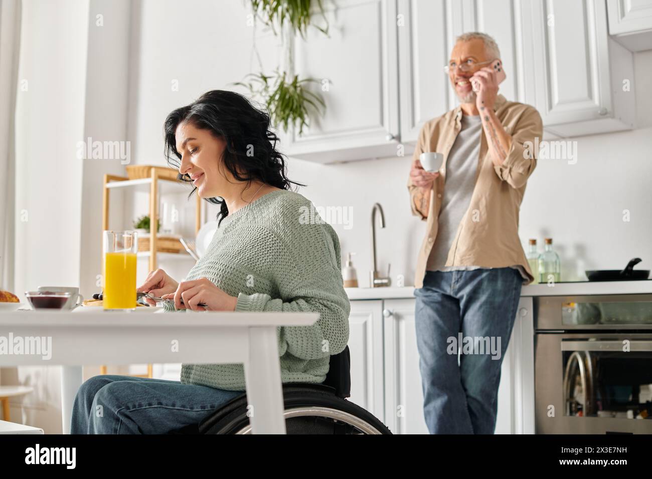 A disabled woman in a wheelchair and her husband together in their home kitchen. Stock Photo