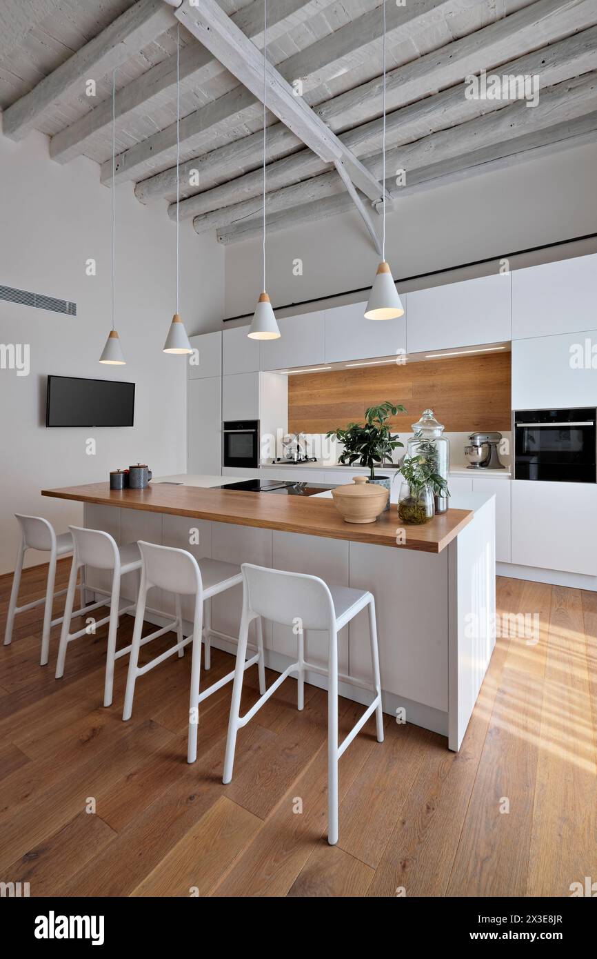 interior view of a modern white kitchen, in the foreground the island kitchen with stools, the lighting is entrusted to four pendant lamps, the floor Stock Photo