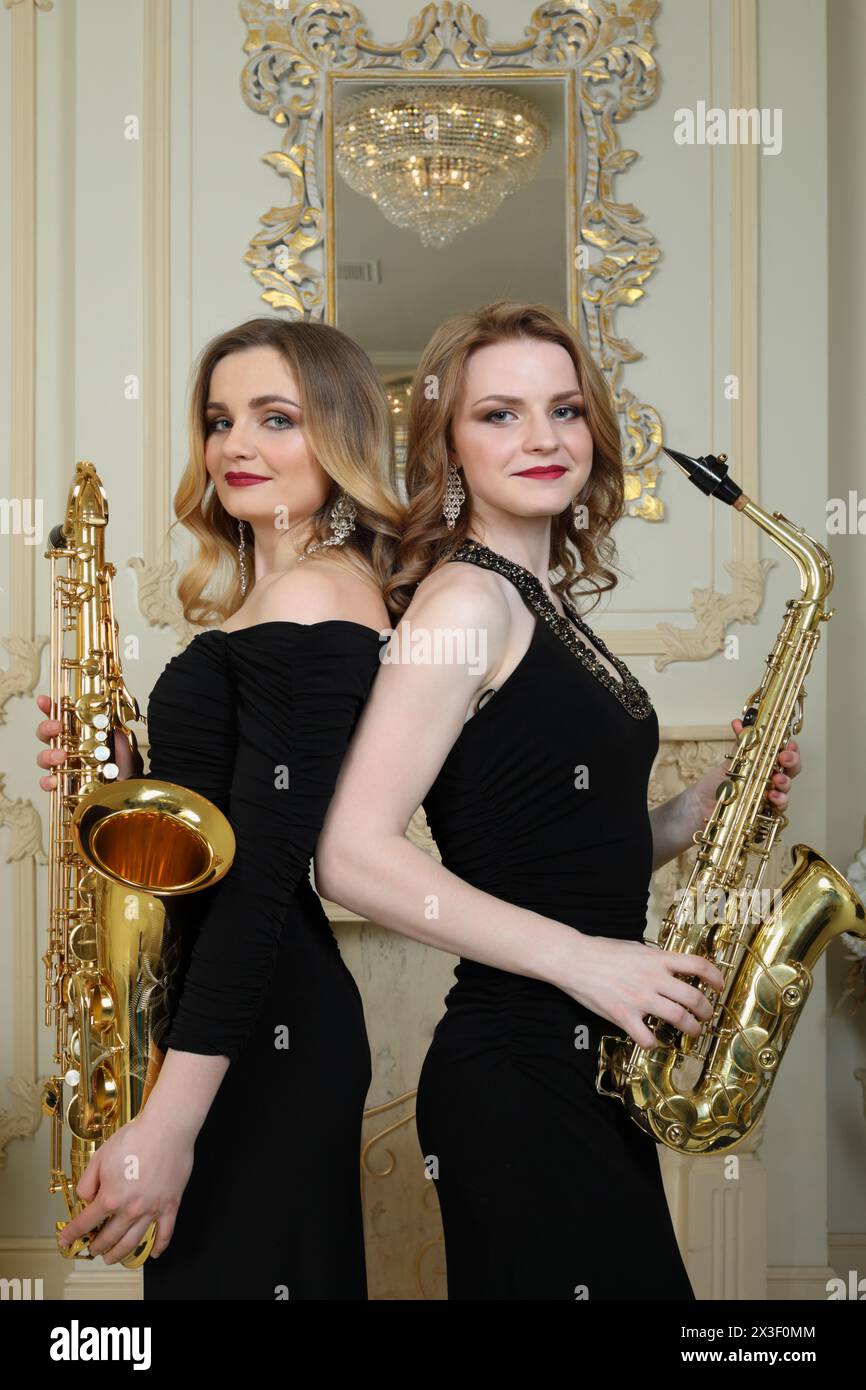 Two women in black stands with saxophones in baroque studio with mirror Stock Photo