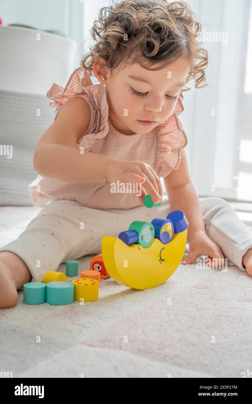 Vertical photograph of a girl playing with wooden balance toy. pieces, colors and different shapes to practice motor skills. Montessori education and Stock Photo