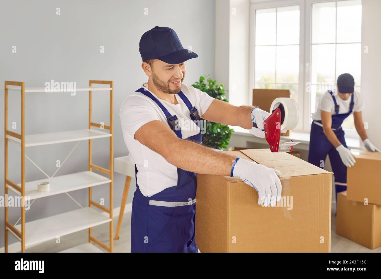 Young skilled male worker of moving service glues cardboard box with