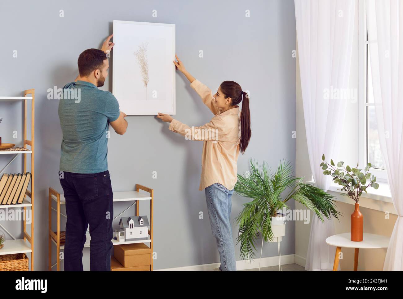 Happy Family Couple Decorating Home And Hanging Picture On Wall Together Stock Photo
