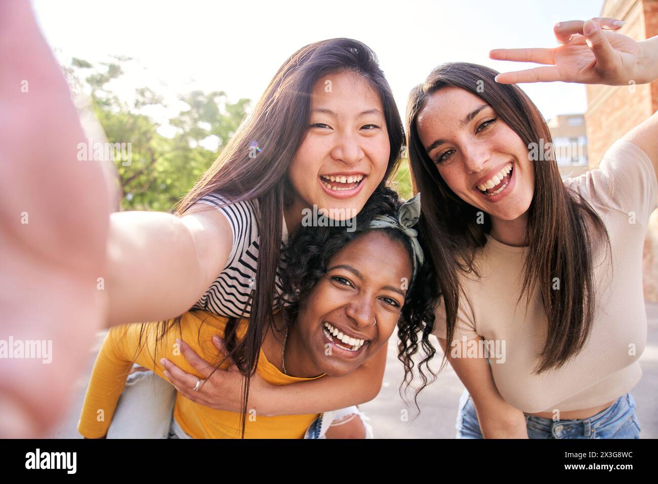 Group young multi-ethnic female taking smiling selfie portrait together outdoors. Excited friends. Stock Photo
