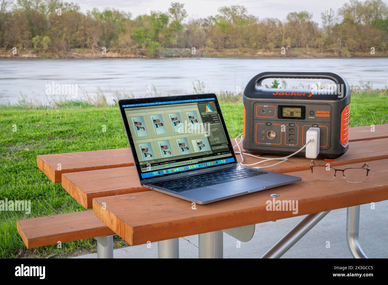 Brownville, NE, USA - April 22, 2024: Editing pictures on MacBook Pro laptop connected to Jackery power station, picnic table on a shore of the Missou Stock Photo