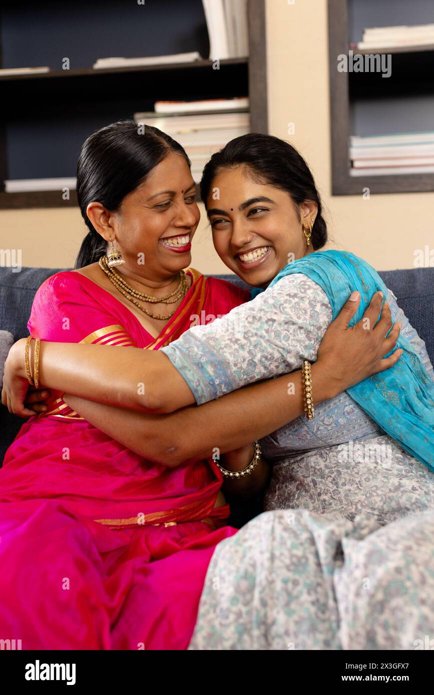Indian mother and teenage daughter in traditional attire, laughing and hugging at home Stock Photo